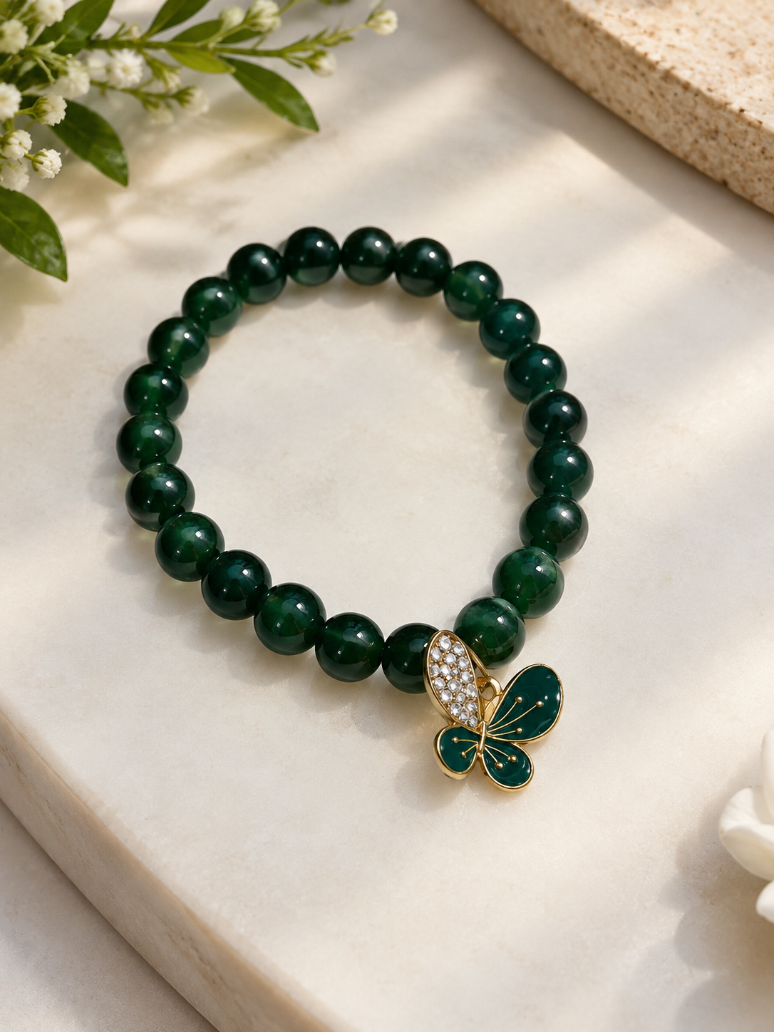 Emerald-green beaded bracelet with a gold butterfly charm on marble